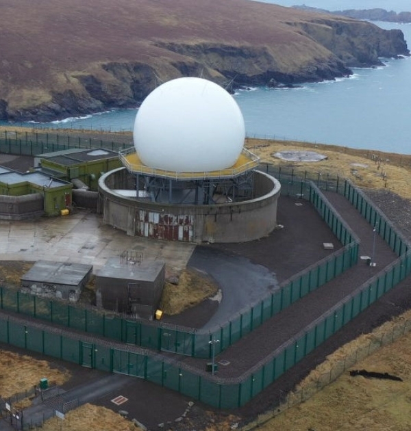 Aerial view of a perimeter security fence surrounding an FCDO government radome facility on a remote coastal clifftop site