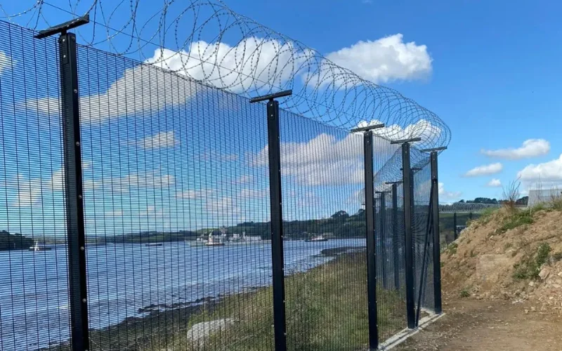 Razor wire concertina security topping installed on high-security mesh fence along a coastal perimeter