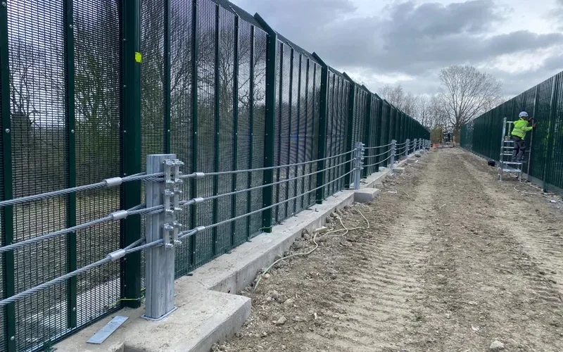 Fence-line hostile vehicle mitigation springline system being installed along a high-security perimeter fence