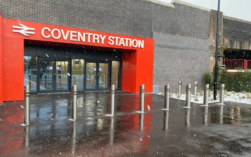 Shallow-mount stainless steel security bollard array protecting the entrance of a UK rail station in winter
